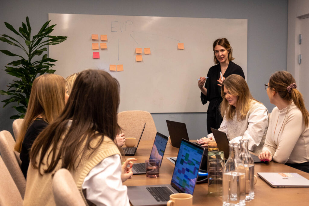 Personer som sitter vid ett bord och står  framför en whiteboard och pratar om att rekrytera en Marketing Automation Specialist.